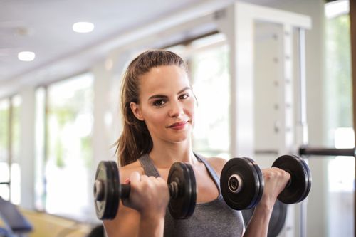 Free Woman exercising with dumbbells in a bright, modern gym, showcasing fitness and strength. Stock Photo