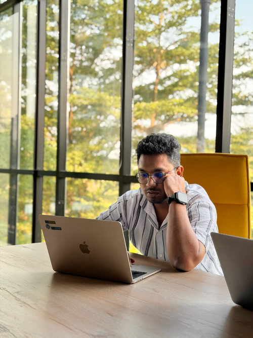 Free Man in striped shirt working on a laptop at a contemporary office with large windows. Stock Photo