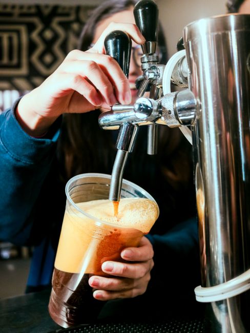 A tall glass of nitro cold brew coffee with a dense tan foam head cascading down the inside of the glass as it settles.