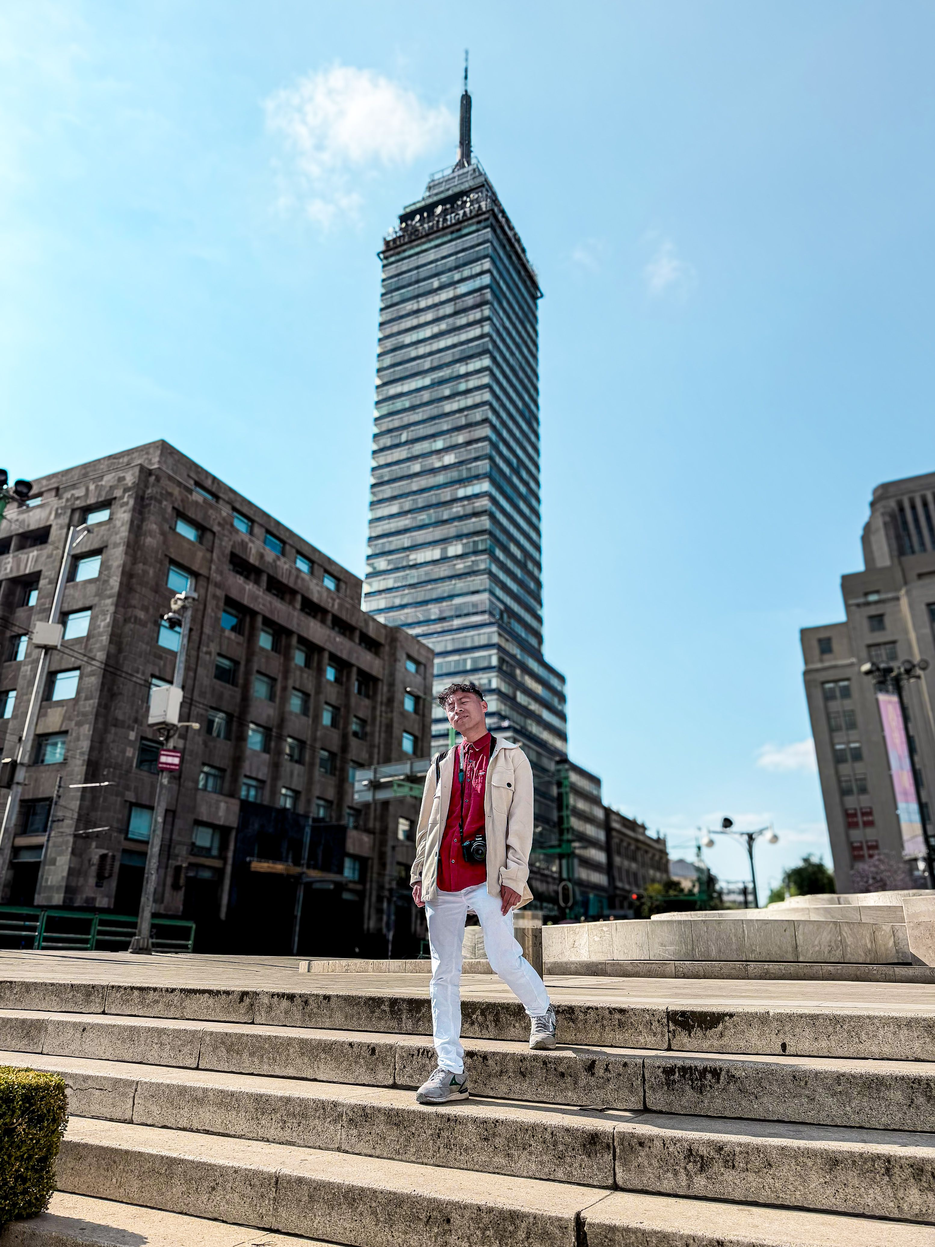 Stylish man on steps with Torre Latinoamericana in the background on a sunny day.