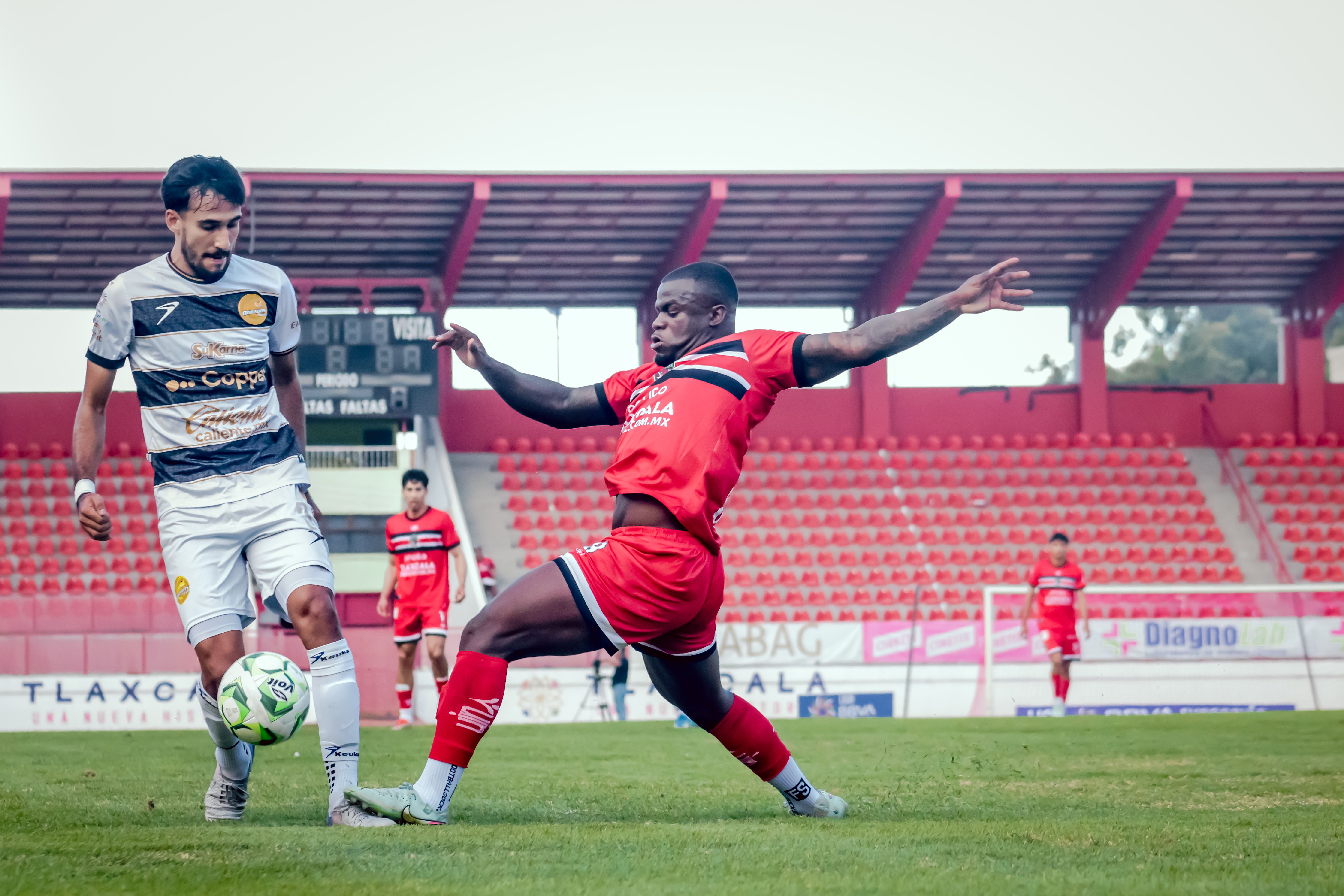 Soccer players in action during an exciting match at a bright red stadium, showcasing athletic prowess.