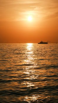 Sunset over calm ocean with a silhouetted ship on the horizon, creating a serene and peaceful atmosphere.