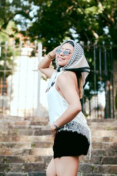 Chic woman wearing scarf and sunglasses, posing outdoors on stone steps in Mexico.