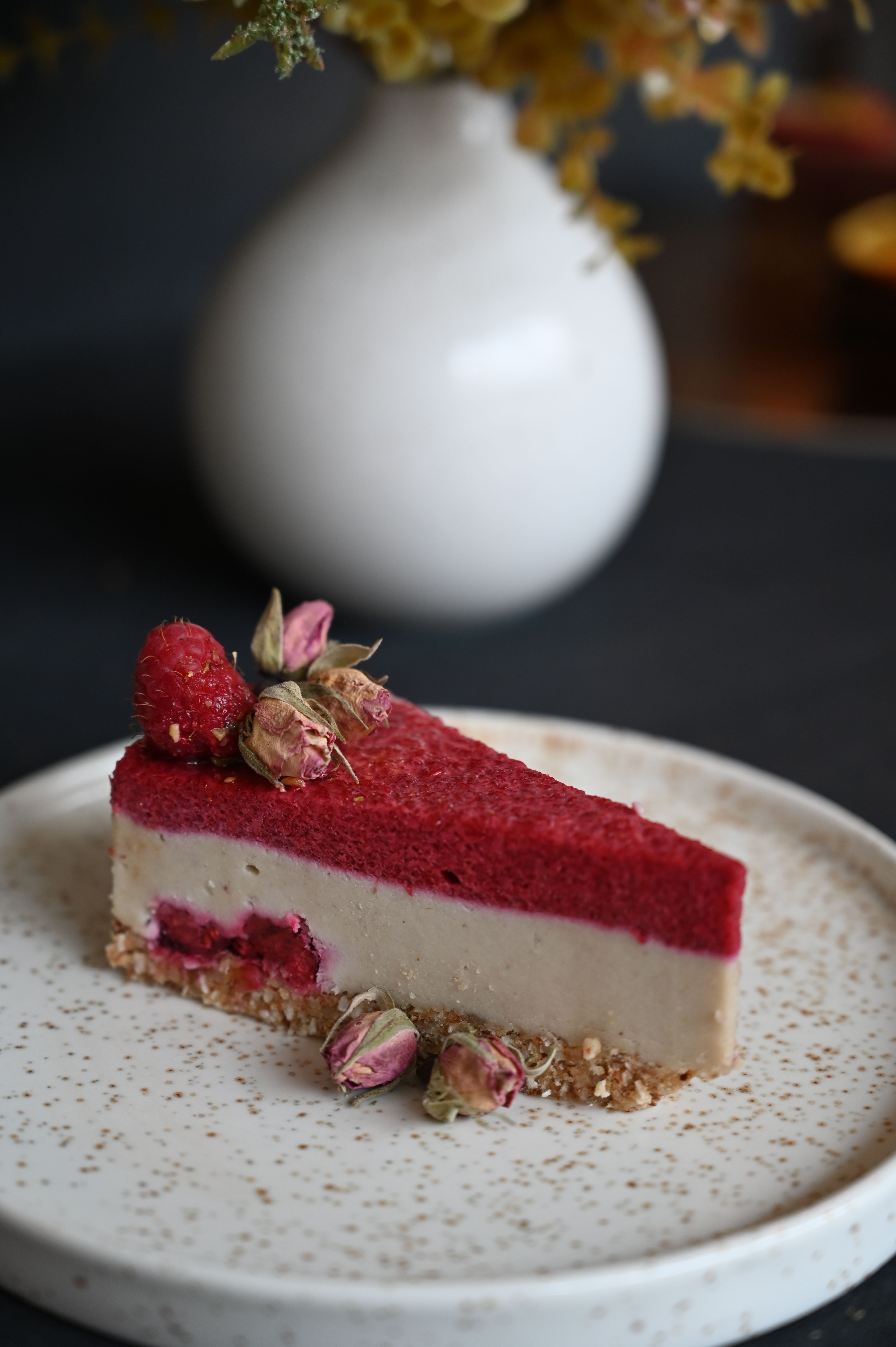 A delicious slice of vegan raspberry cheesecake served elegantly on a speckled ceramic plate.