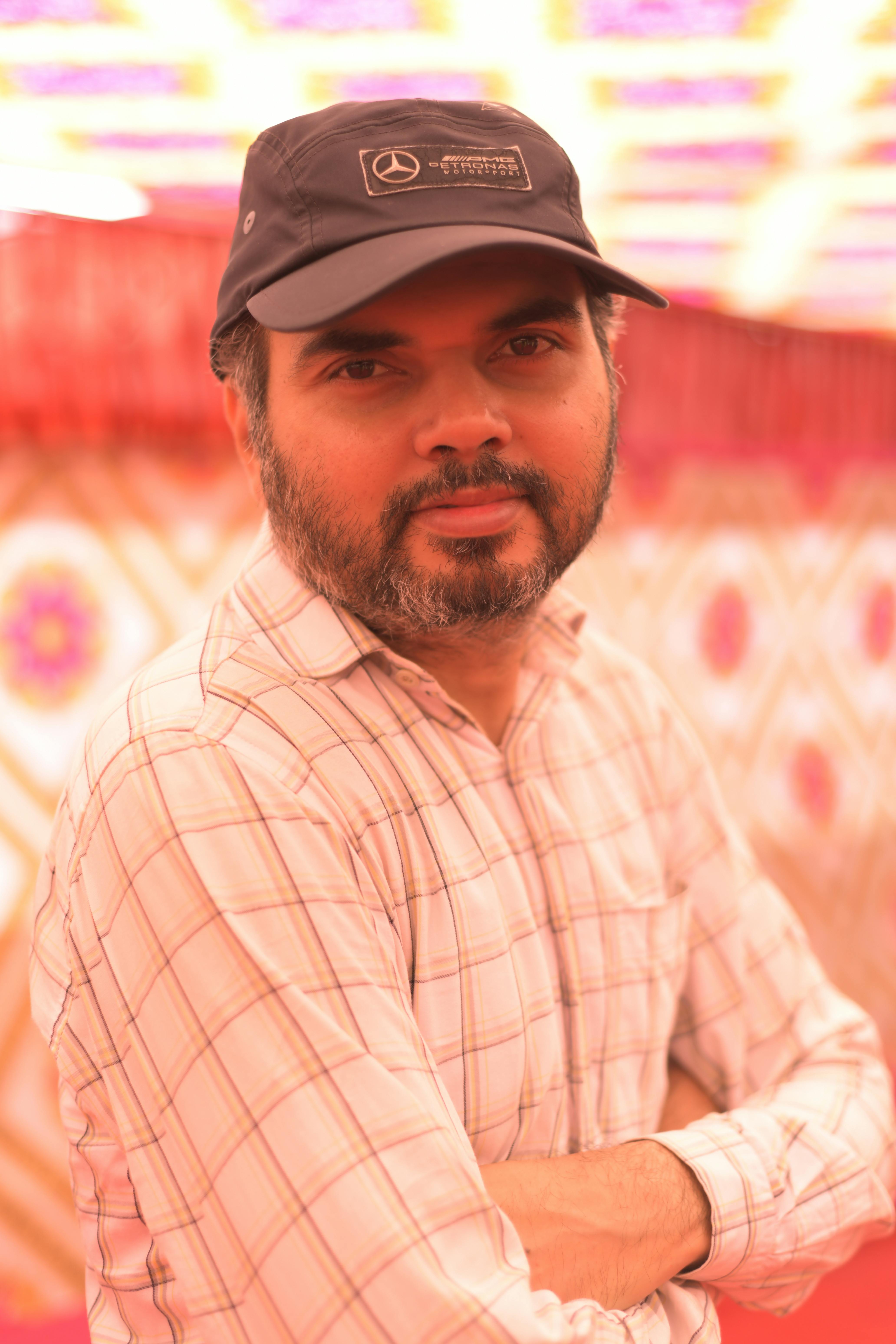 A middle-aged man with a beard and cap poses indoors with a patterned background.