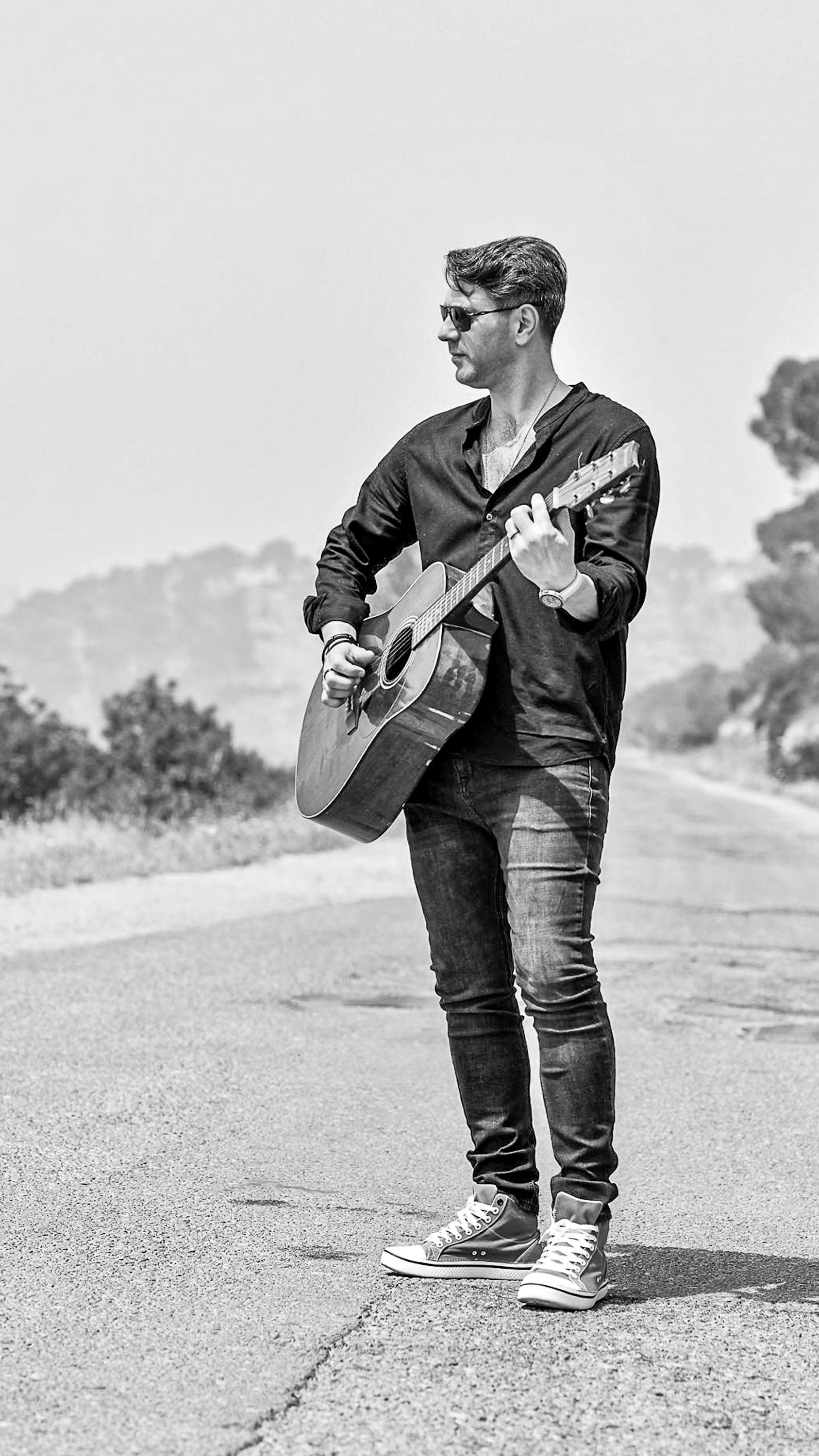 A man playing acoustic guitar on a sunny road, showcasing musical freedom.