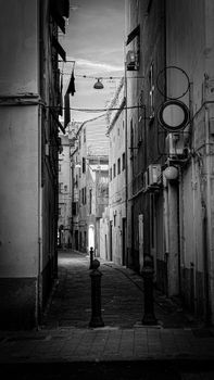 Black and white image of a narrow, historic alleyway in Genoa, Italy, showcasing classic architecture.