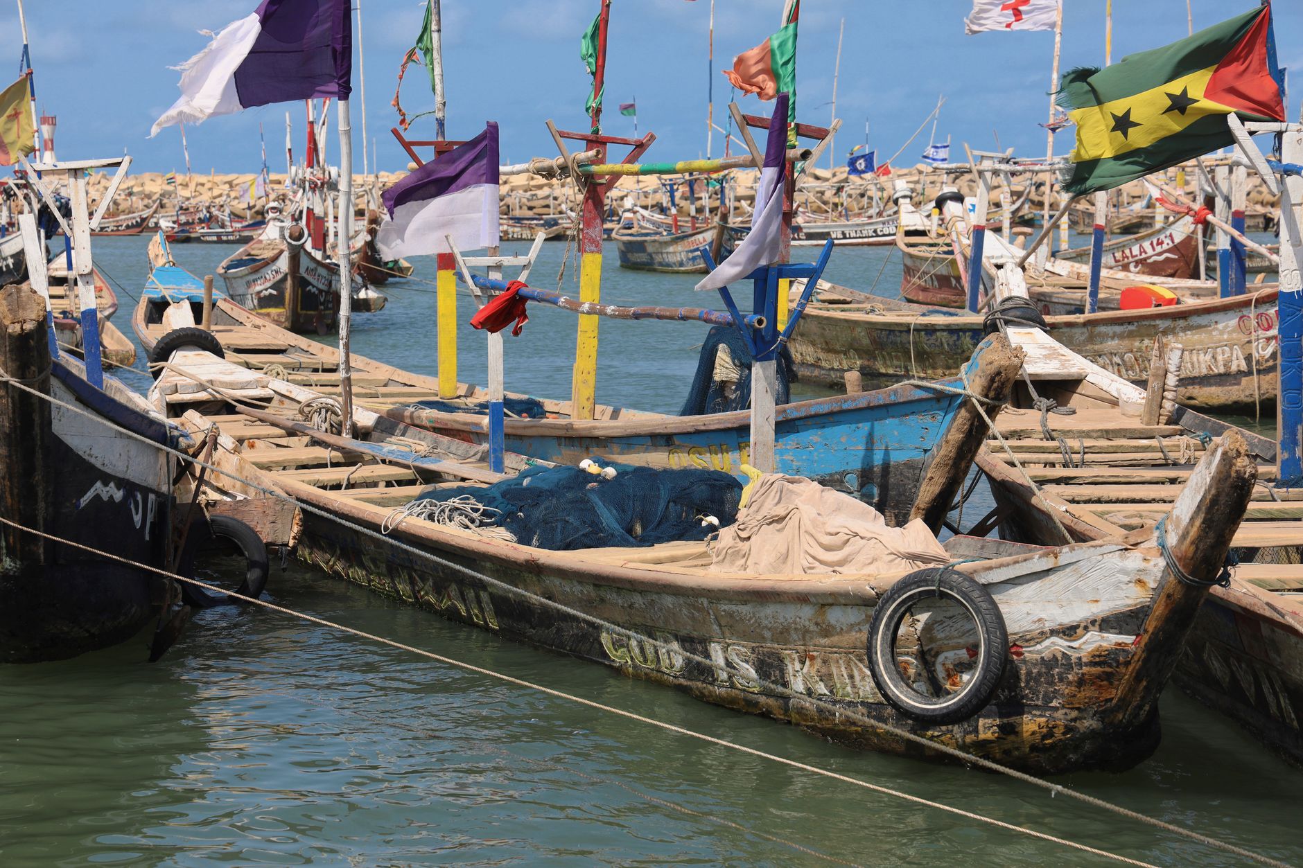 Colorful traditional fishing boats docked at the harbor in Accra, Ghana displaying various flags.