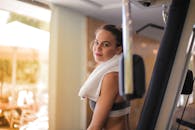 一位年轻女子脖子上围着毛巾在健身房锻炼，散发着健康和健美的气息