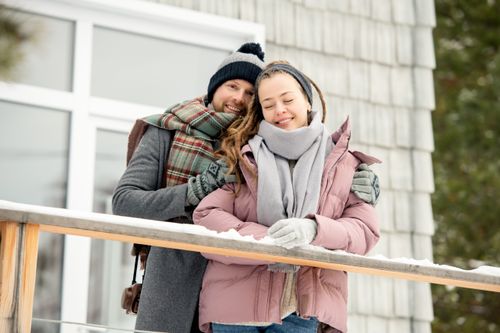 Free Happy couple embracing during winter on a balcony with snowy surroundings. Stock Photo