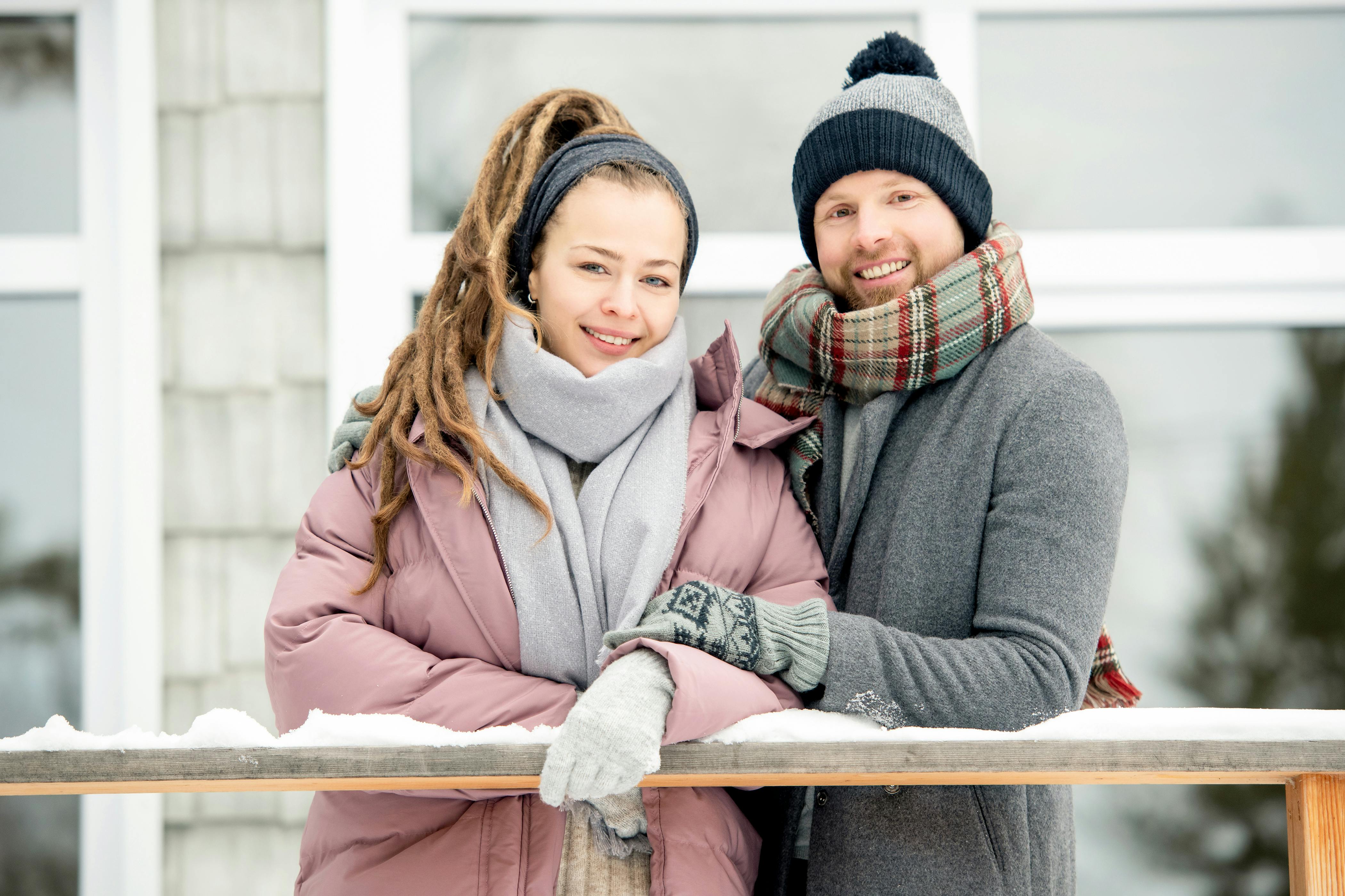 一对夫妇微笑着，在户外戴着围巾、穿着温暖的冬装，一起享受冬天