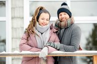 一对夫妇微笑着，在户外戴着围巾、穿着温暖的冬装，一起享受冬天