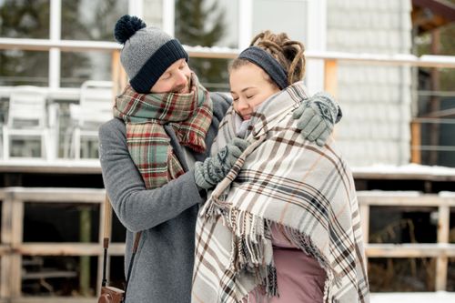 Free Couple embracing warmly with scarves and blankets in a winter setting. Capture of affection and togetherness. Stock Photo