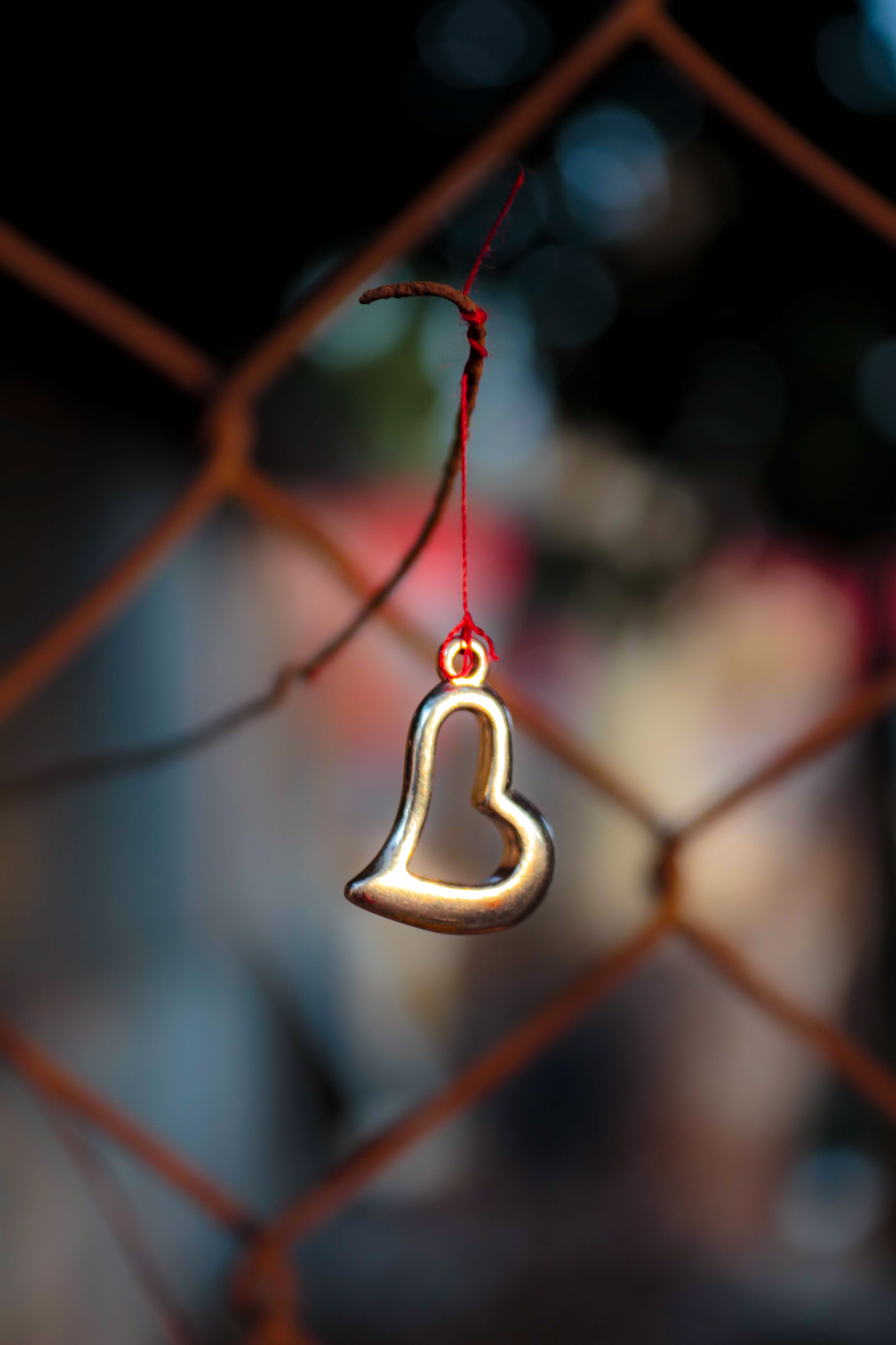 A heart metal charm on a red string against a blurred background, symbolizing love.