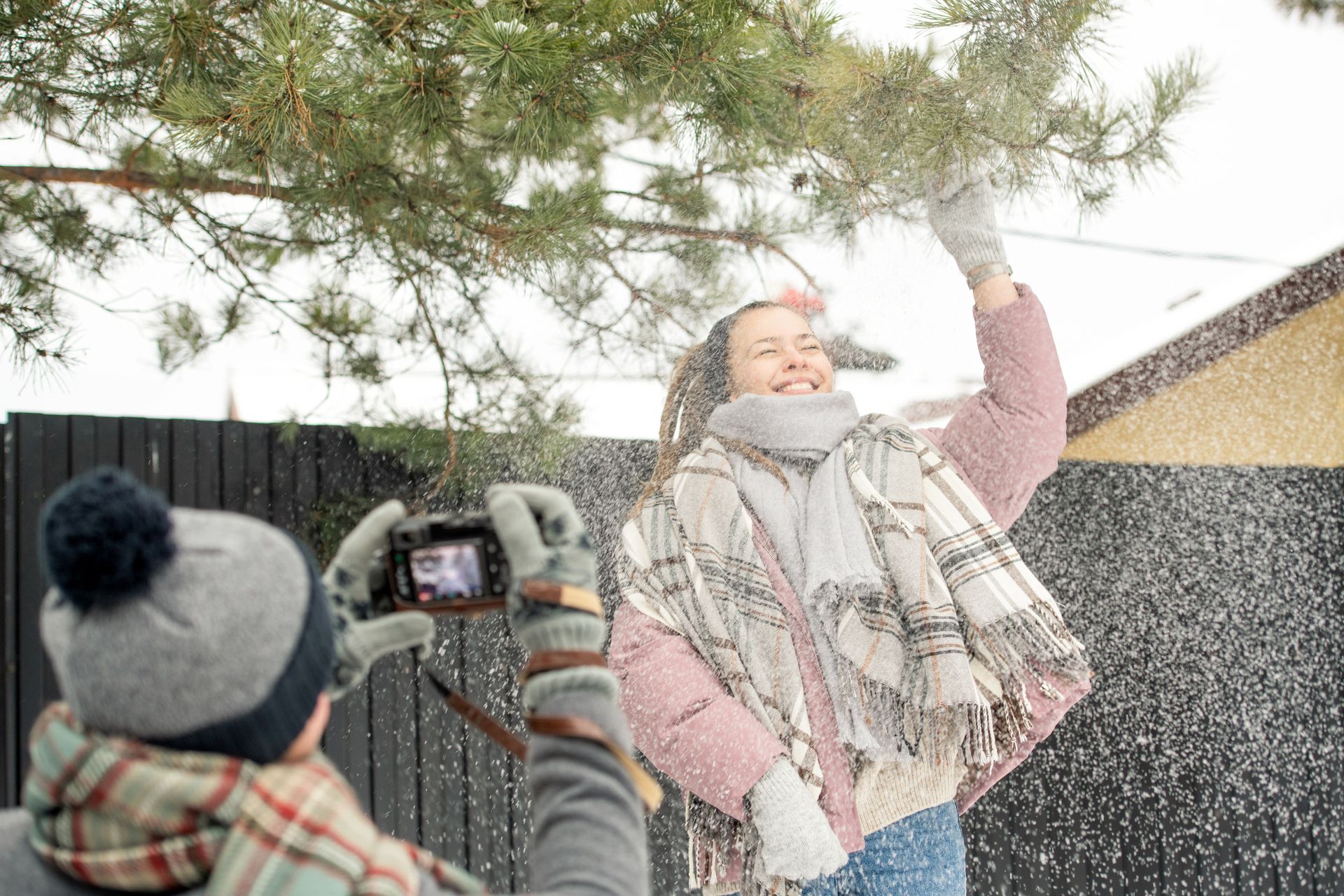Capturing joyful moments outdoors in winter, playing with snow under a pine tree.