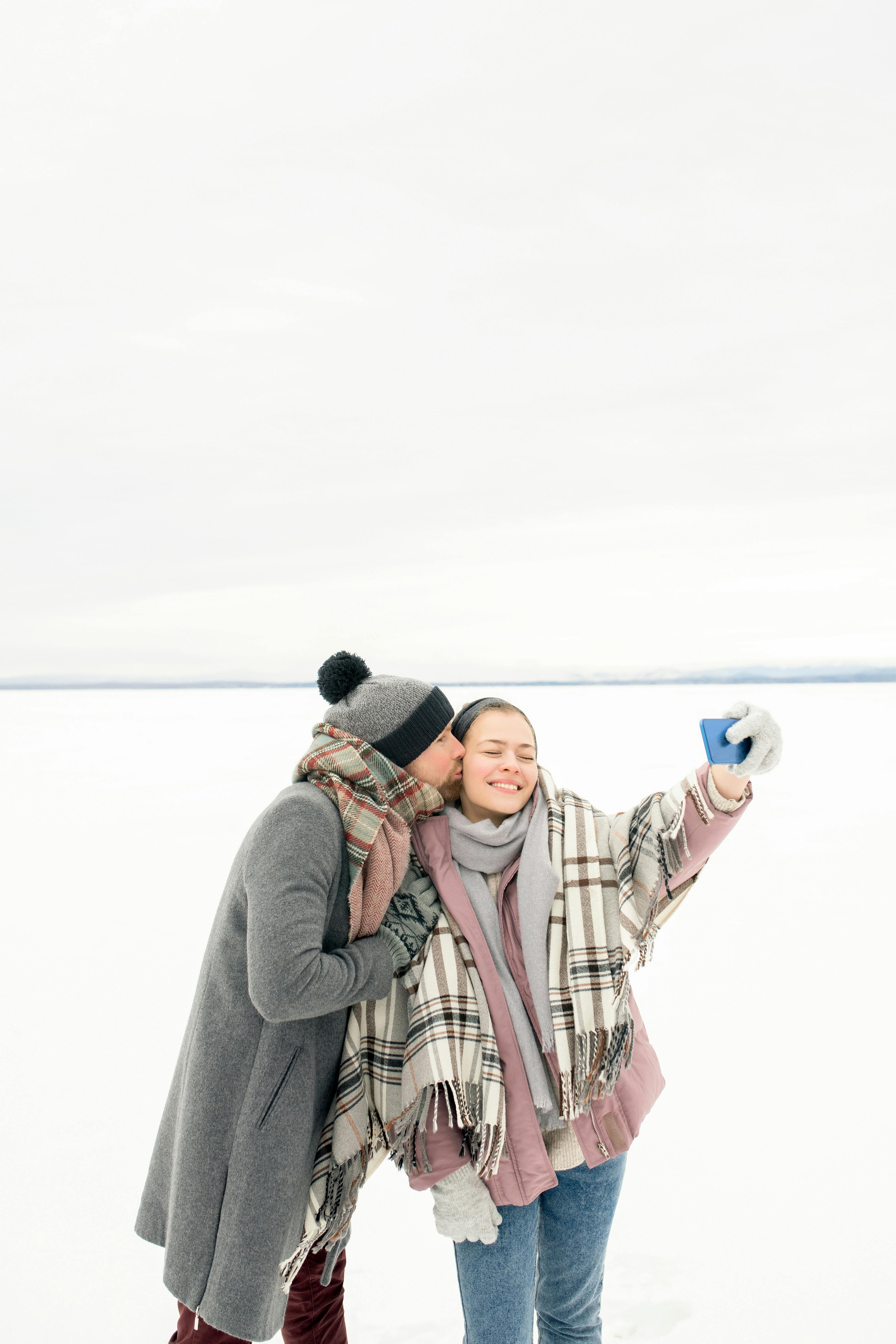 一对快乐的夫妇在白雪皑皑的冬日户外自拍，他们围着围巾，显得很温暖