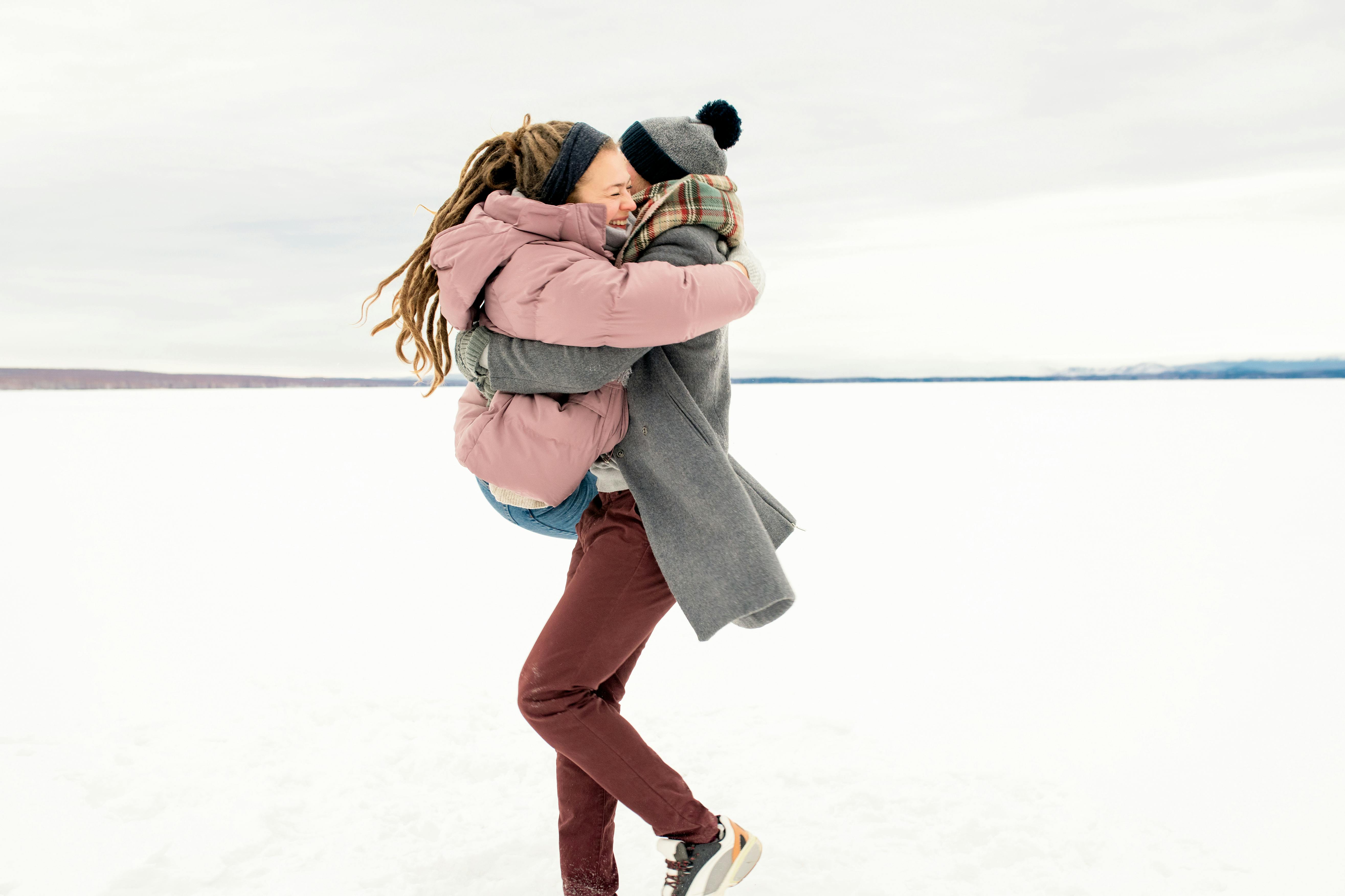 冬日白雪皑皑的户外，一对夫妇快乐地相拥，衣着温暖，神情幸福