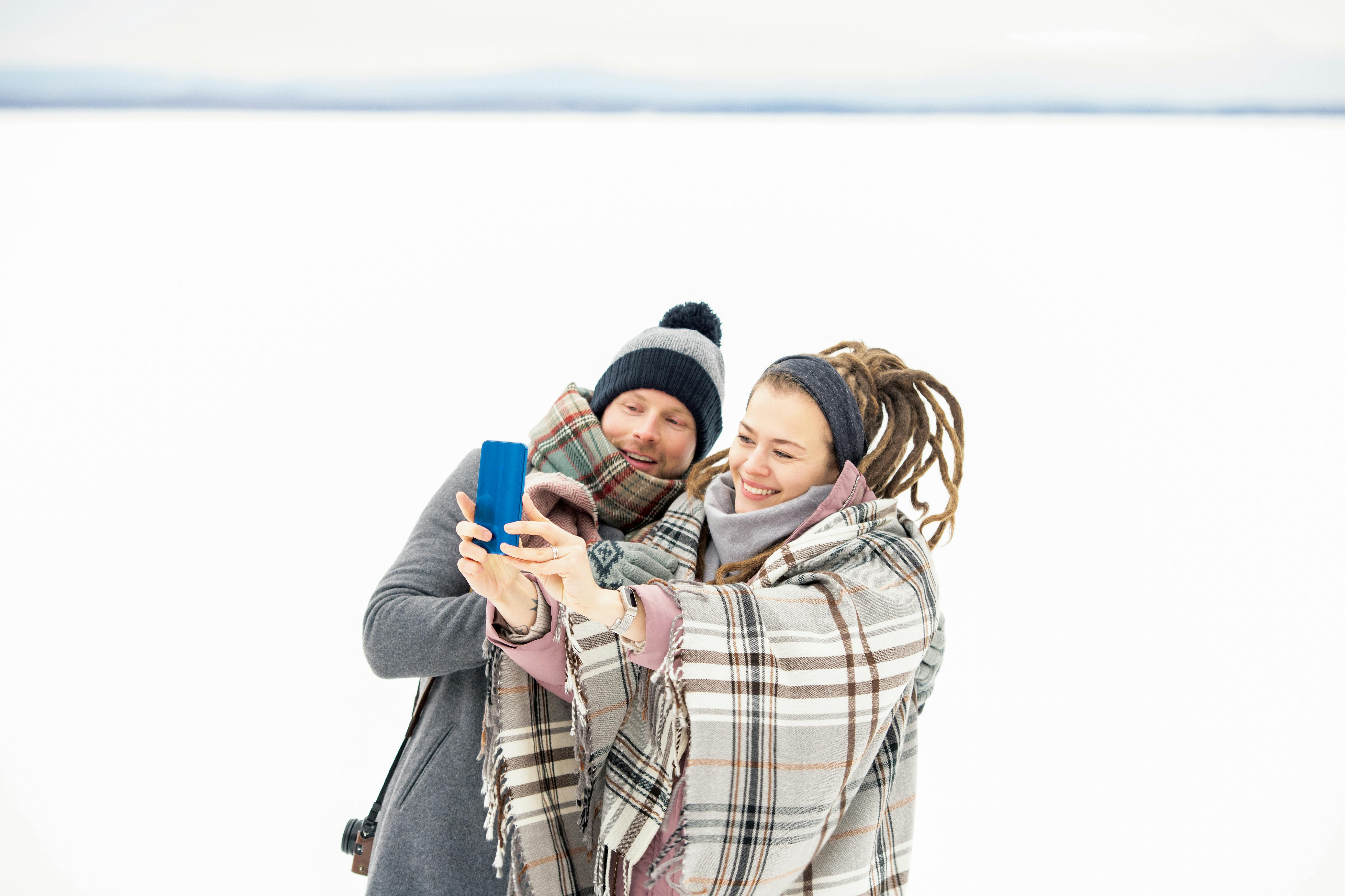 一对情侣穿着冬装，在白雪皑皑的背景下微笑着自拍