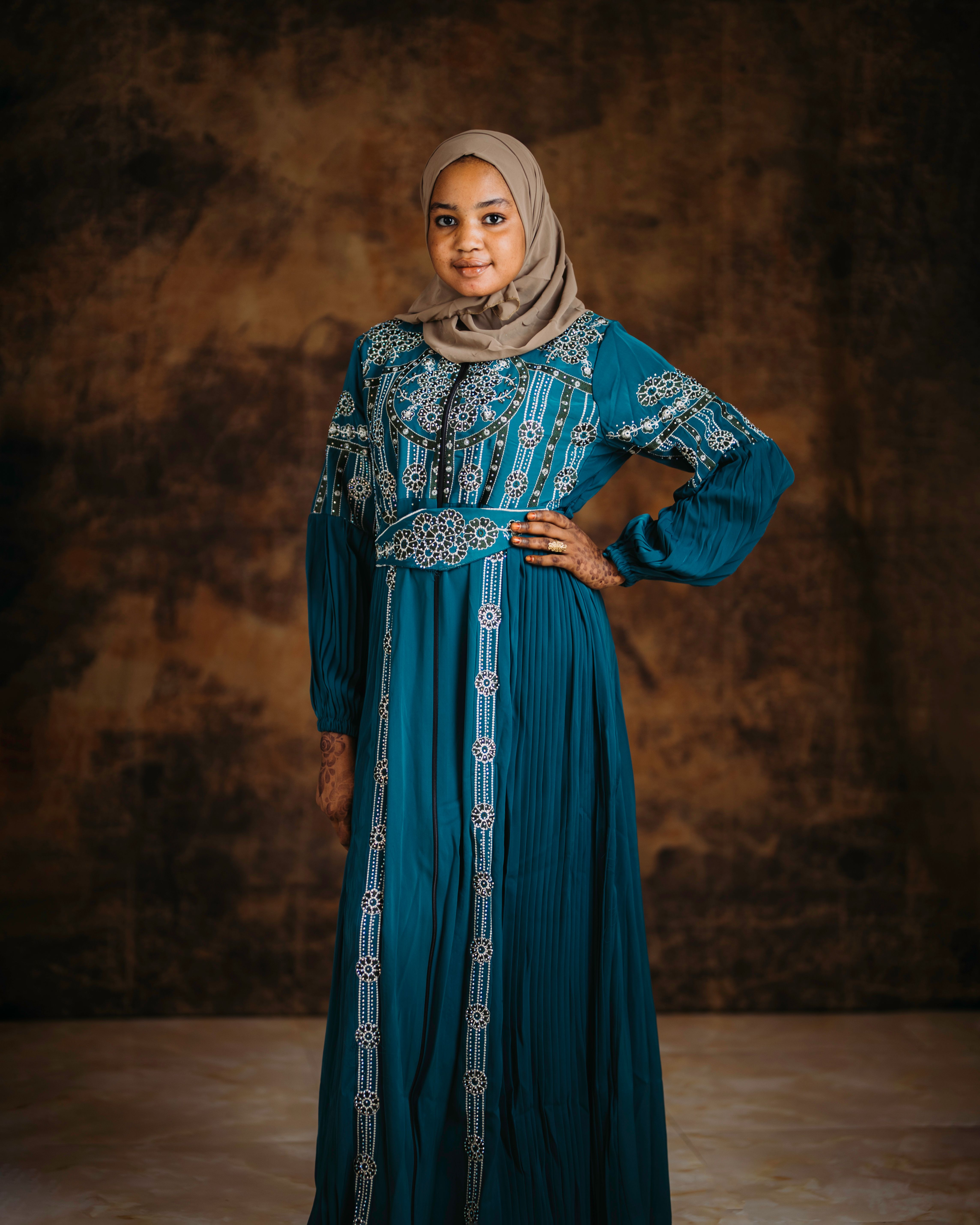 Portrait of a woman in a blue traditional dress with intricate designs, against a textured background.