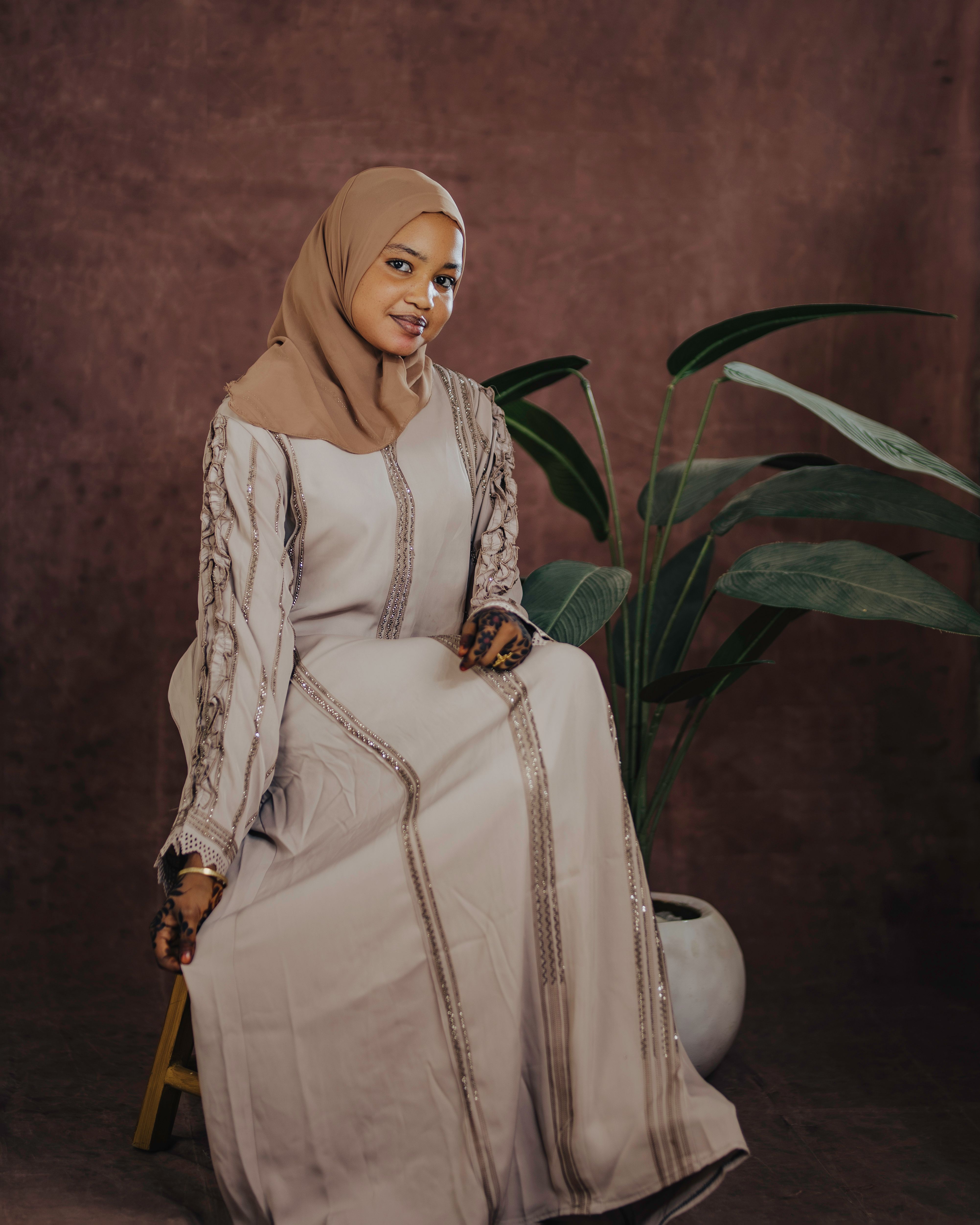 A seated woman in traditional attire with a plant backdrop, exuding elegance and calm.