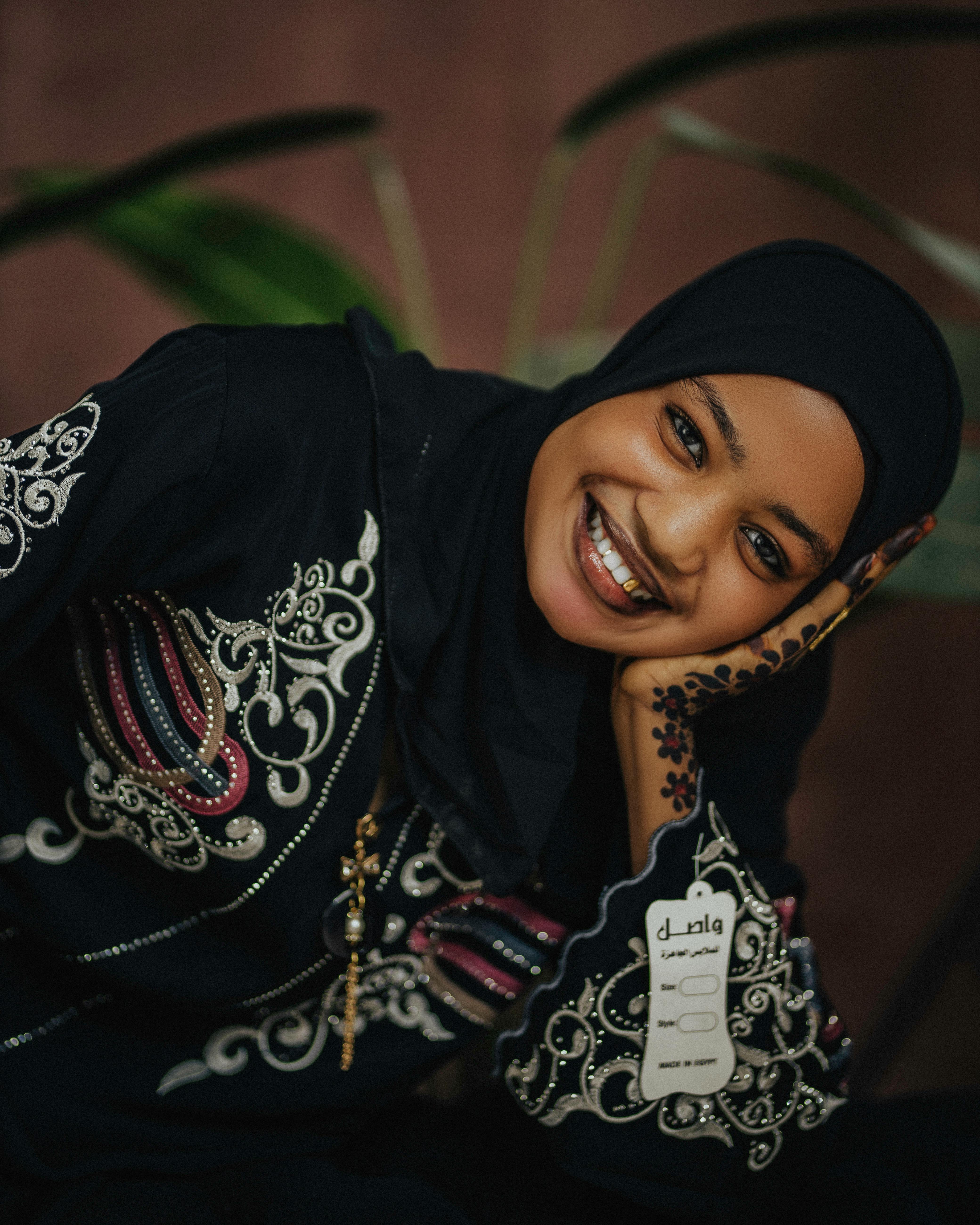 Woman in intricate embroidered attire, smiling with henna artwork on hand.