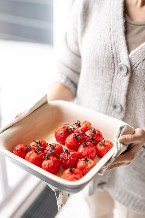 Free A woman in a cozy sweater holds a tray of freshly roasted red cherry tomatoes on the vine. Stock Photo