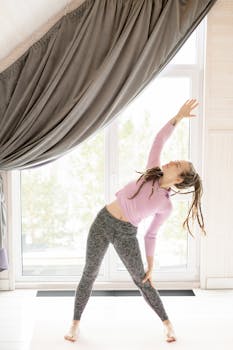 Woman doing a stretch exercise in a sunlit room with large windows and curtains.