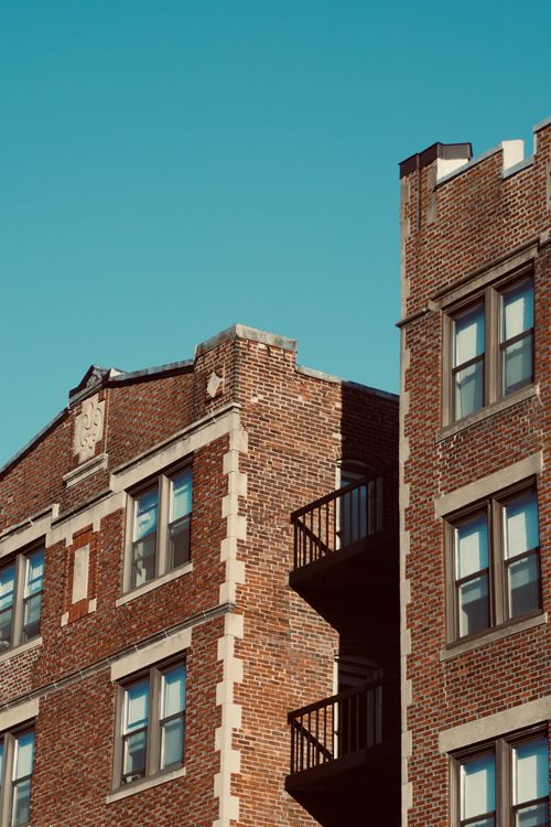 Free Charming brown brick apartment building with classic architectural details against a clear blue sky. Stock Photo
