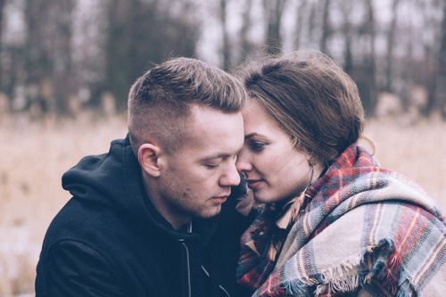 Free A loving couple wrapped in plaid, sharing a tender moment in an outdoor fall setting. Stock Photo