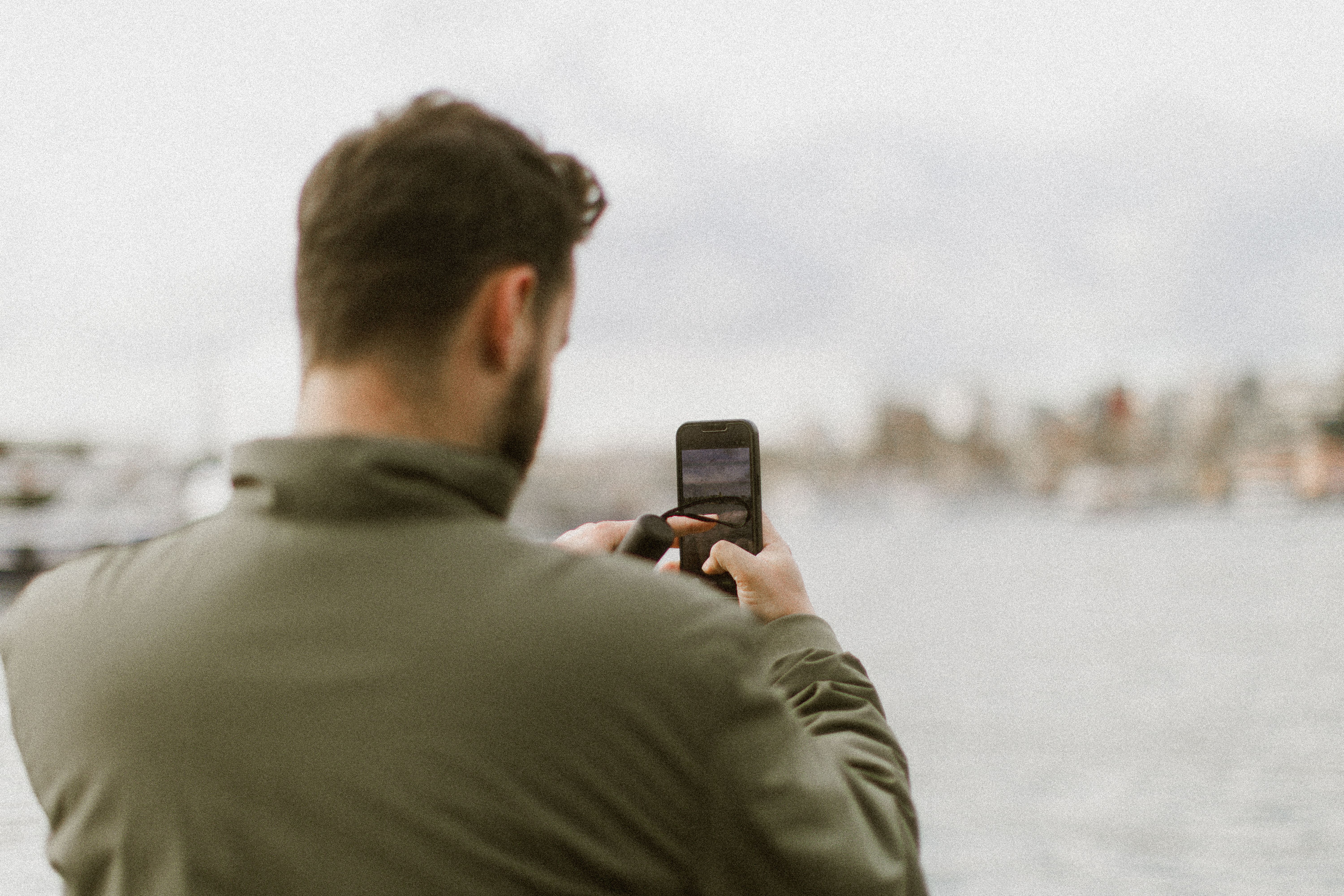 A man captures a scenic waterfront view using his smartphone, highlighting a casual and modern lifestyle.