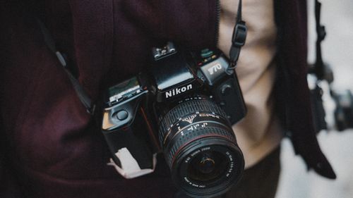 Free Close-up of a photographer holding a classic Nikon film camera, capturing street life outdoors. Stock Photo
