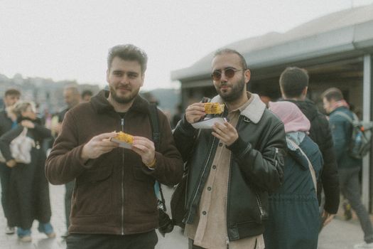 Two men savor roasted corn at an outdoor market in Istanbul, Turkey, showcasing local culture.