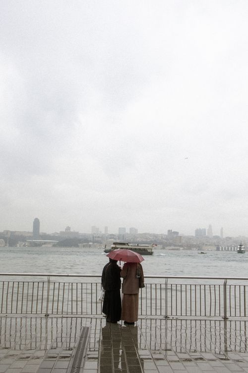 Free A couple stands under an umbrella by the Istanbul waterfront on a cloudy day. Stock Photo