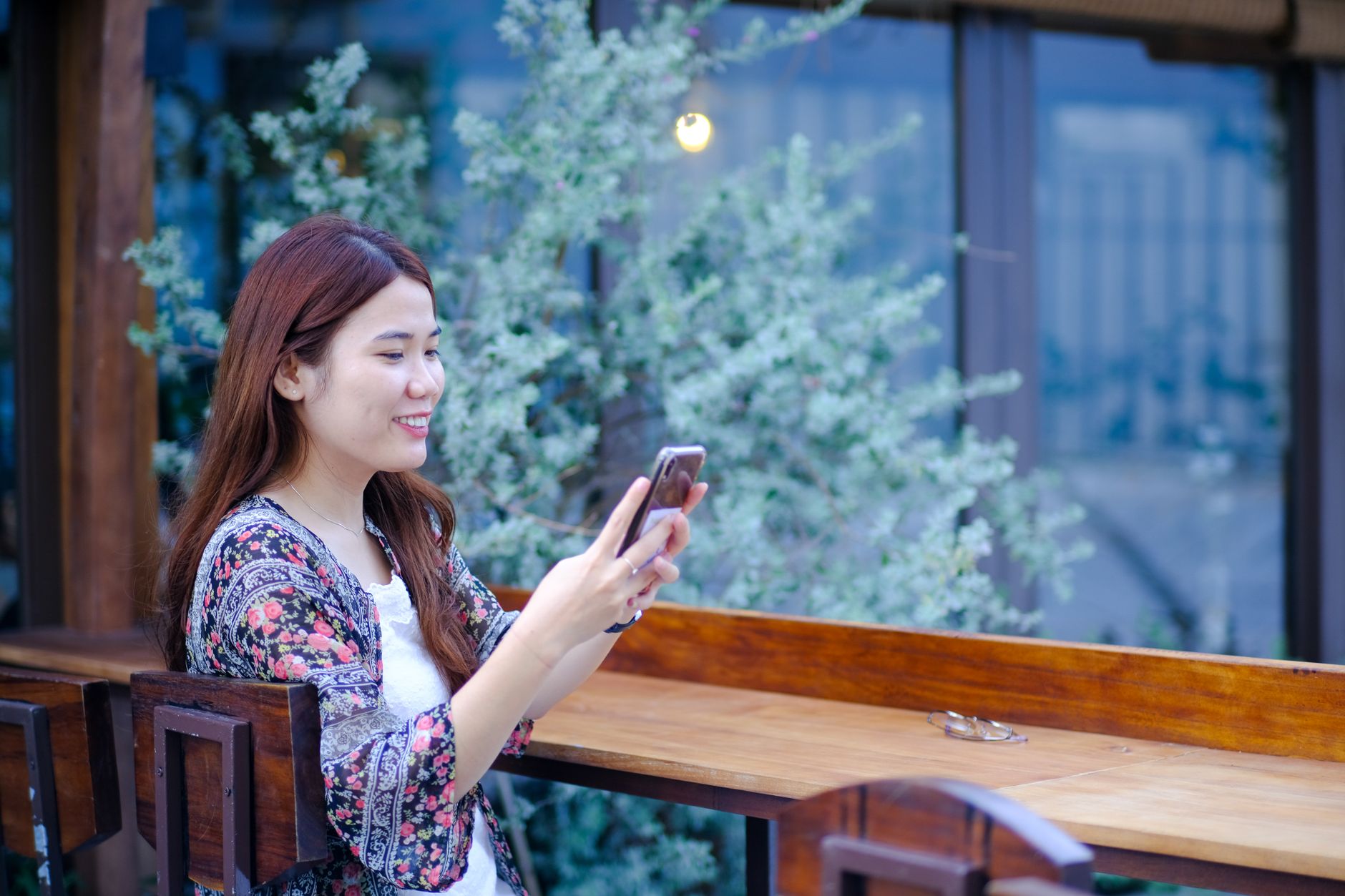 A smiling young woman uses her phone outdoors in a peaceful setting in Da Nang, Vietnam.