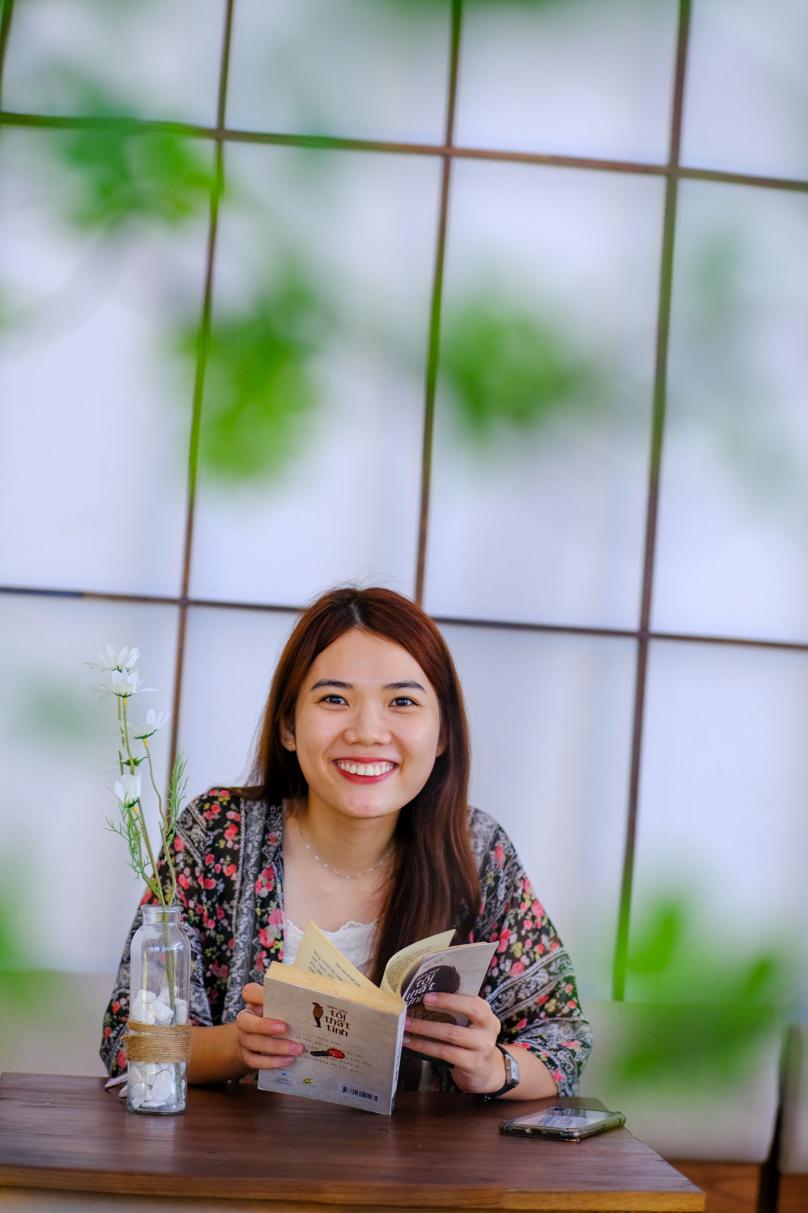Asian woman enjoying a book in a cozy Da Nang café with natural decor.