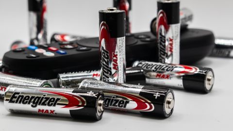 Close-up of multiple Energizer AA batteries and a remote control on a white surface.