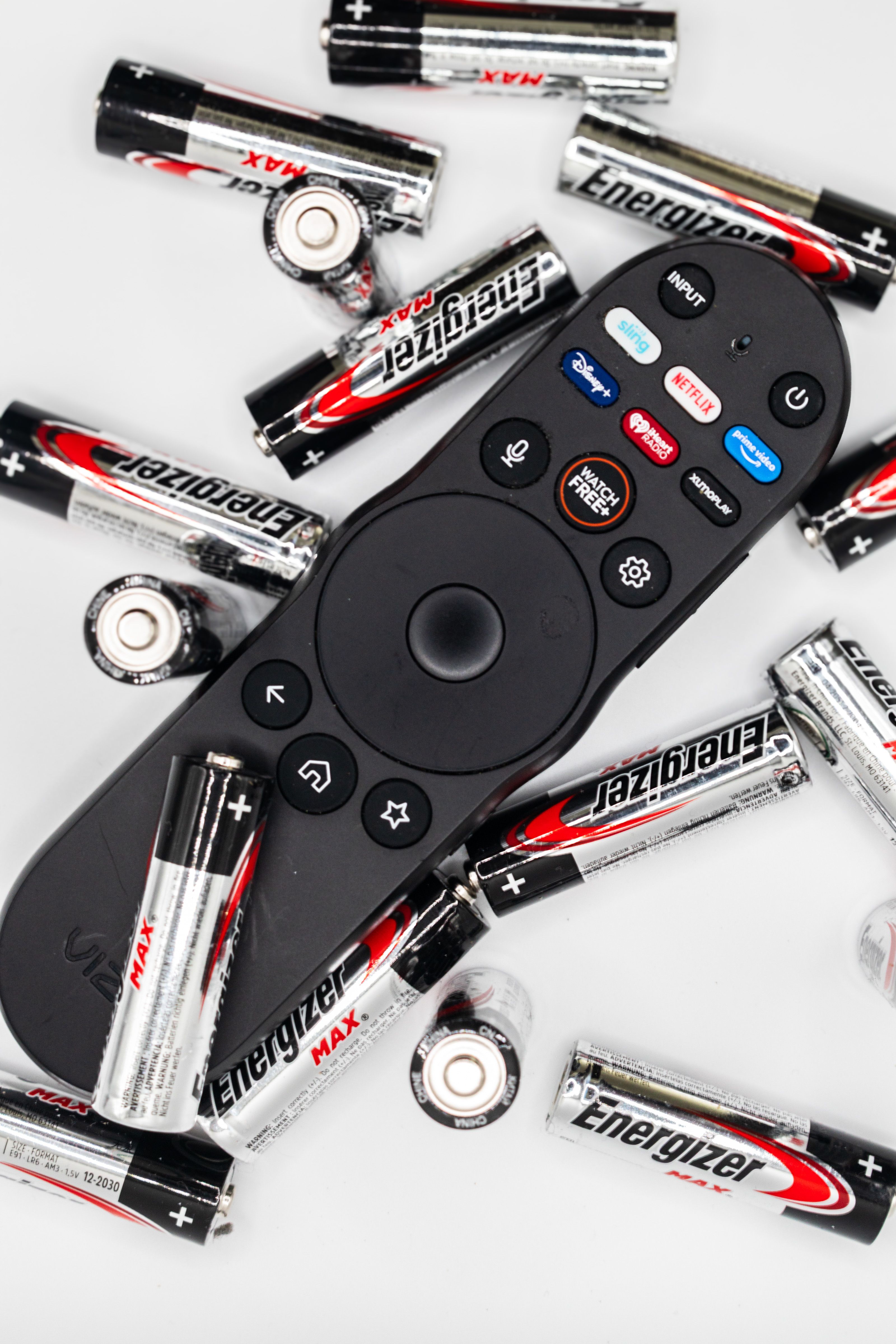 Black remote control surrounded by AA batteries on a white surface.