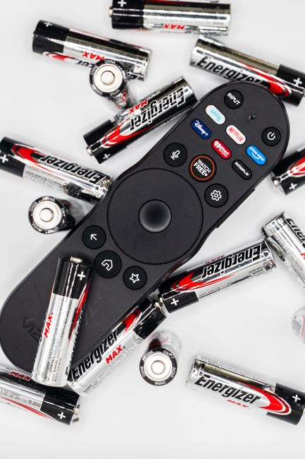 Black remote control surrounded by AA batteries on a white surface.