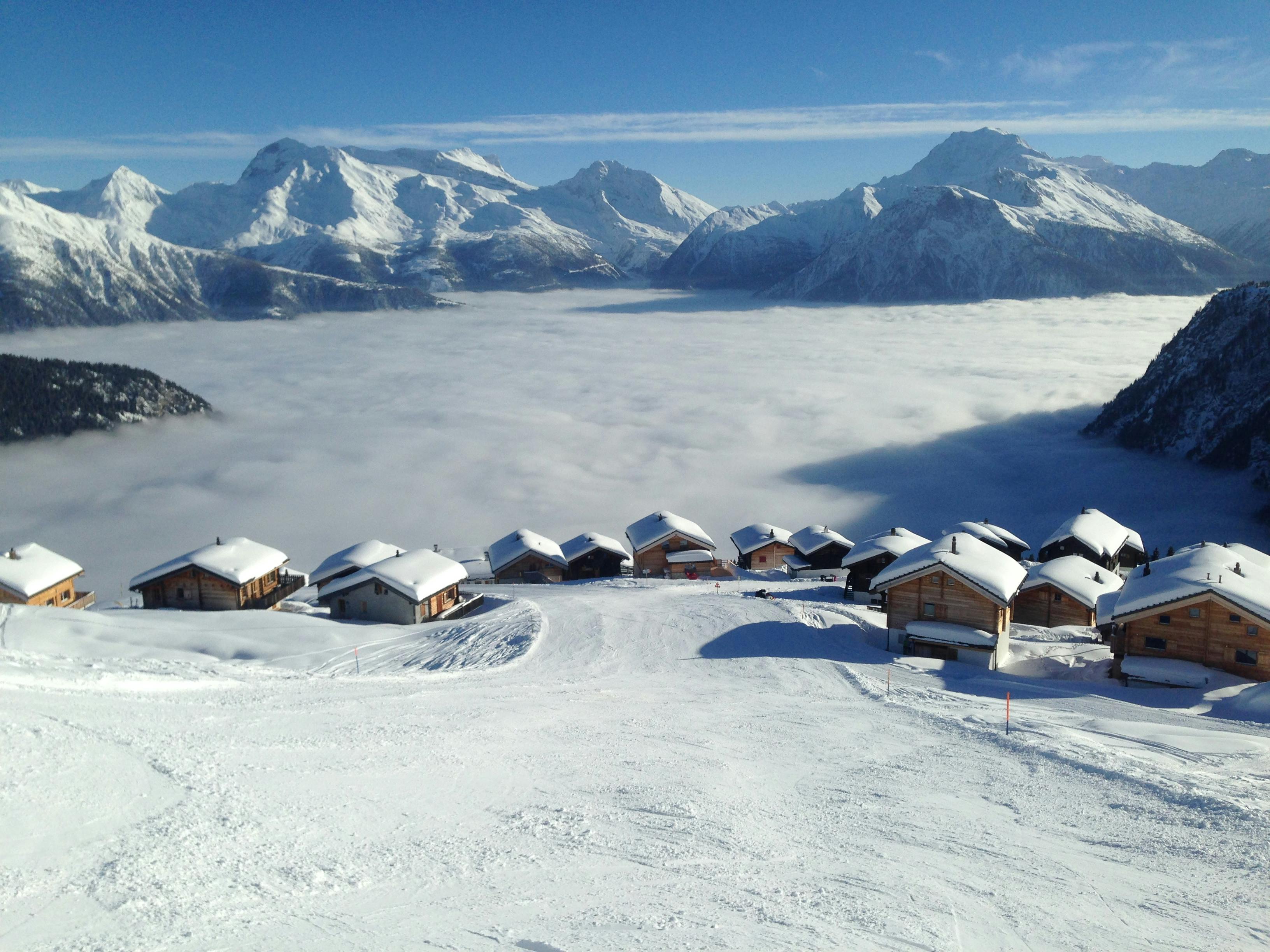 Prescription Goggle Inserts - Idyllic snow-covered village nestled in majestic alpine mountains with misty clouds below.