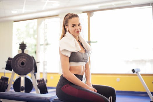 年轻女子在健身房锻炼后，脖子上围着毛巾，微笑着坐着