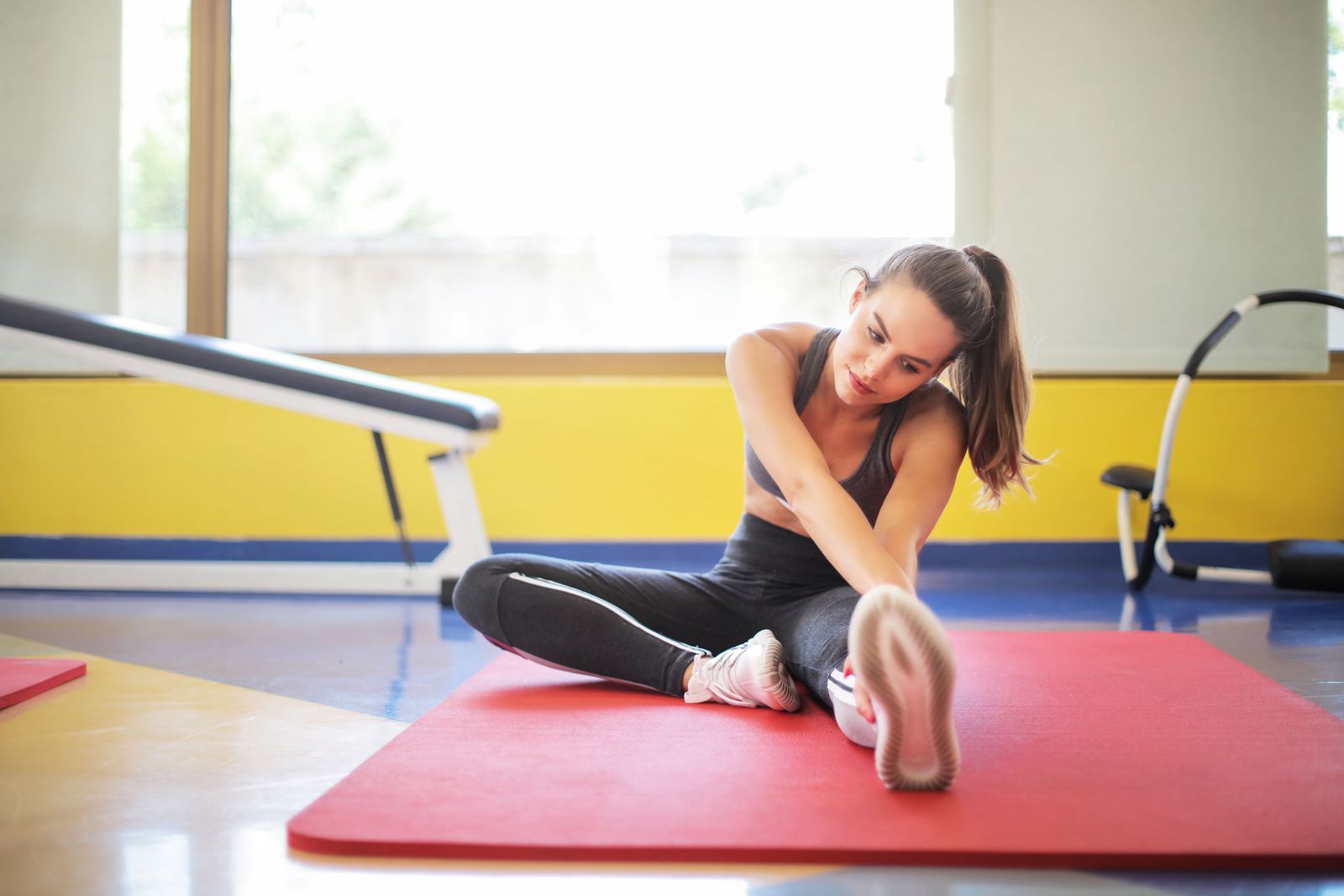 Woman stretching on a yoga mat in a bright studio, working on hamstring and hip flexibility