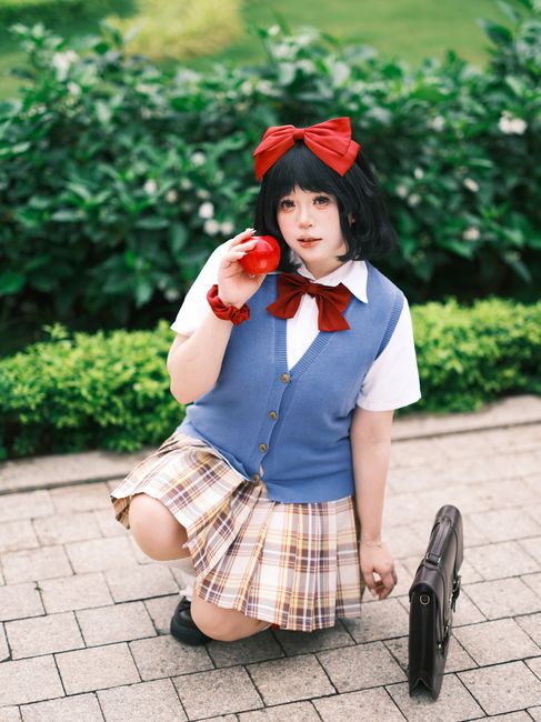 Young woman in anime cosplay outfit kneeling outdoors with a red apple.
