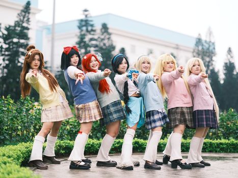 Seven young cosplayers pose in colorful anime-inspired costumes outdoors, exuding excitement and creativity.