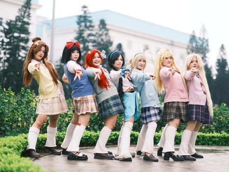A group of seven cosplayers dressed in anime attire posing confidently outdoors.