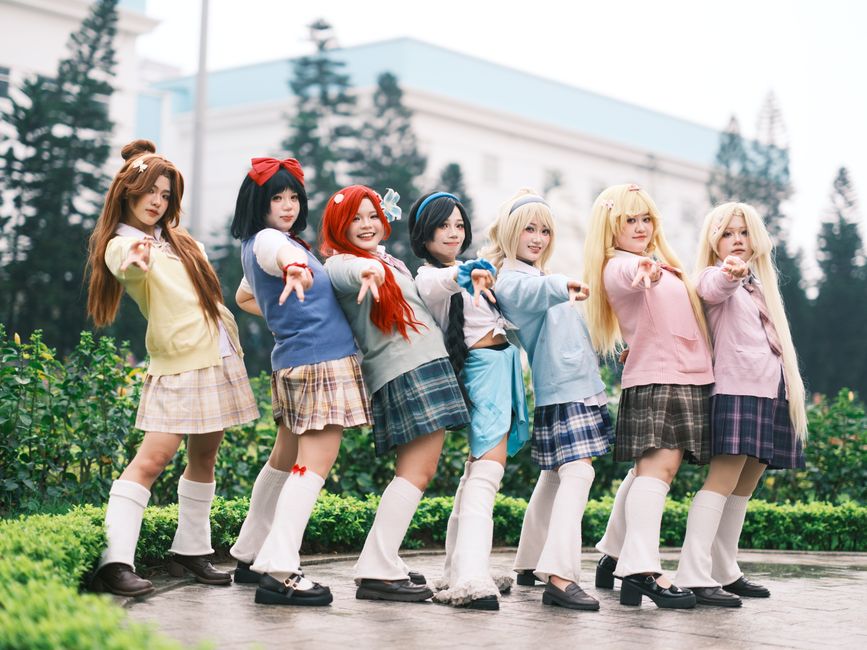 アニメの衣装に身を包んだ7人のコスプレイヤーが、屋外で自信満々にポーズをとっている。