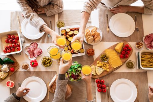 Free Top view of a family toasting at a lunch table with cheese, olives, and fresh salads. Stock Photo