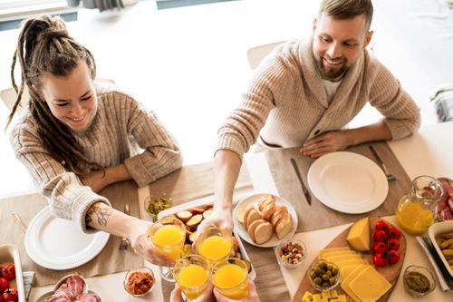 Free A joyful breakfast scene with friends toasting with orange juice around a table of food. Stock Photo