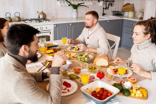 Free Cozy indoor gathering of friends at a table set with diverse dishes and orange juice. Stock Photo