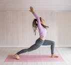 一名女子穿着运动服，在室内的粉色垫子上练习瑜伽