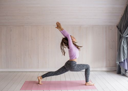 Free A woman in activewear performs a yoga pose on a pink mat indoors, promoting wellness and fitness. Stock Photo